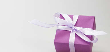 Lila Geschenk mit weißem Geschenkband vor hellem Hintergrund