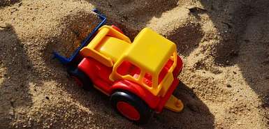 Kleiner bunter Spielzeugbagger, der im Sand steht