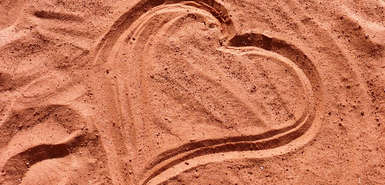 Mit dem Finger gemaltes Herz im Sand